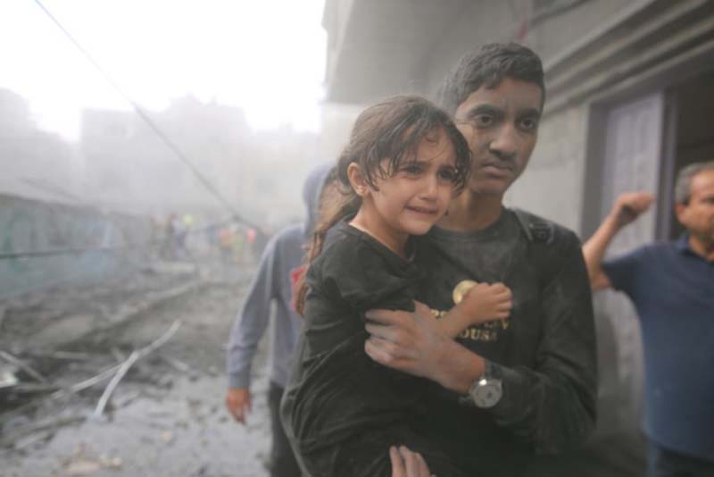 加薩南部城市拉法12日的空襲後，驚魂未定的小女孩被抱離廢墟。圖／取自新華社